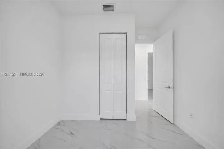 Polished tile flooring with veined detailing, white bi-fold closet doors, and interior paneled doors with satin nickel hardware
