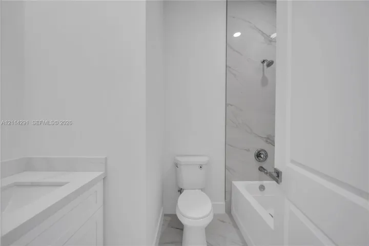 Bathroom featuring a vanity with a stone-surface countertop, tub-shower combination with full-height stone-look tile surround, and tile flooring