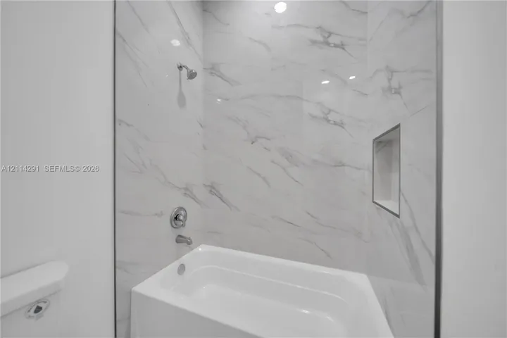 Full-height shower surround with large-format veined tile, integrated recessed shelving, and a polished chrome finish shower-tub faucet assembly