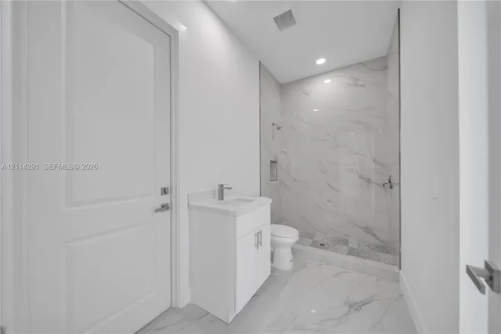 Bathroom featuring large-format tile flooring, a white vanity with a solid-surface countertop, and a walk-in shower with floor-to-ceiling stone-finish tile surround and built-in recessed shelving