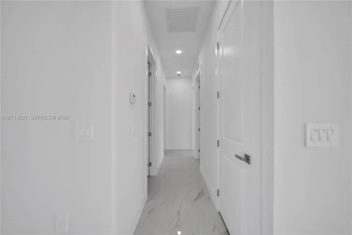 Hallway featuring large-format tile flooring with marble-style veining, recessed LED lighting, and multi-panel interior doors with brushed nickel hardware