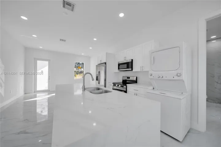 Kitchen featuring stone-finish countertops, a central island with an undermount sink, white cabinetry, stainless steel appliances, and large-format flooring