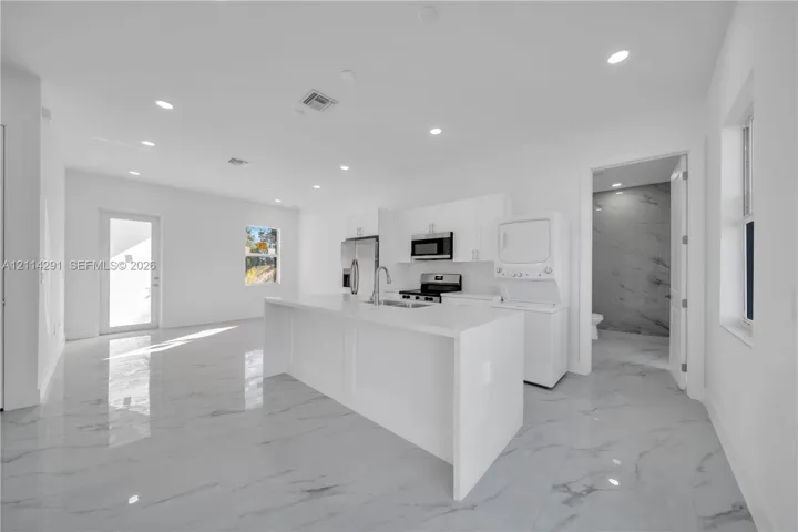 Kitchen featuring a waterfall island with stone countertop, stainless steel appliances, white cabinetry, and stone-finish flooring with recessed lighting