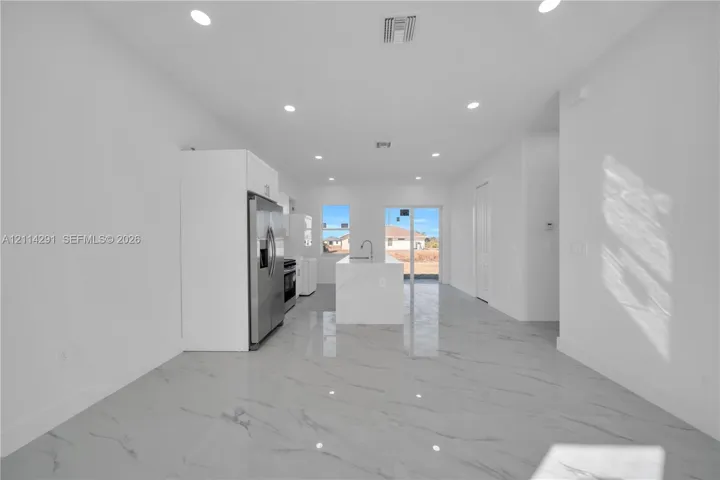 Kitchen featuring large-format tile flooring, quartz-surfaced center island with undermount sink, stainless steel appliances, white cabinetry, and recessed lighting
