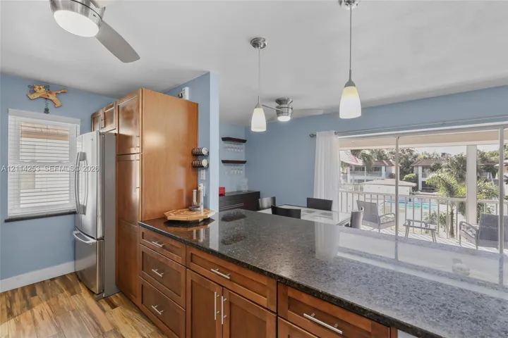 Kitchen featuring wood cabinetry, stone countertops, stainless steel refrigerator, dual pendant lighting, and wood-finish flooring