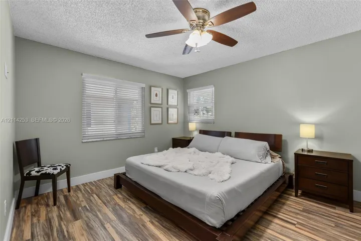 Bedroom featuring wood-finish flooring, a ceiling fan with integrated lighting, and dual windows equipped with horizontal blinds