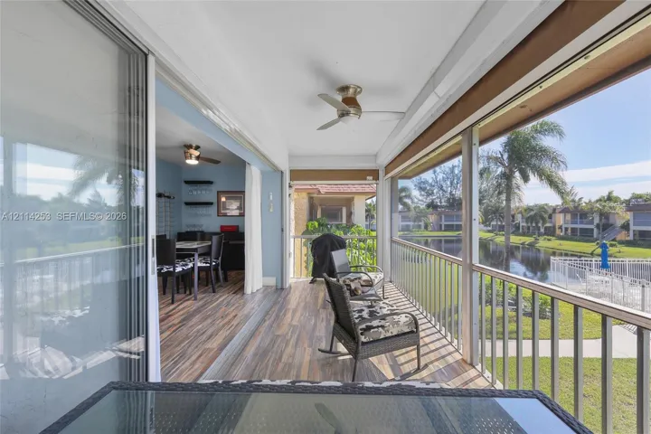 Screened lanai featuring wood-finish flooring, metal railings, and a ceiling fan, opening to a waterfront setting