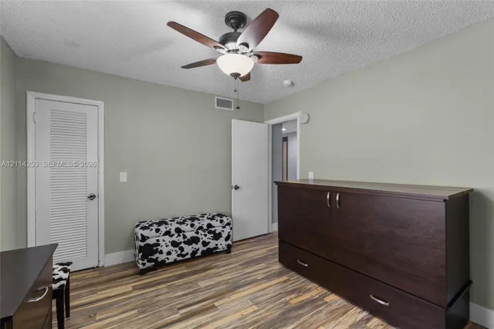 Interior space featuring wood-finish flooring, a ceiling fan with integrated light fixture, and a louvered door