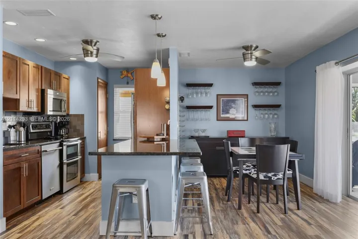 Kitchen featuring wood cabinetry, stone-finish countertops, stainless steel appliances, wood-finish flooring, and dual ceiling fans
