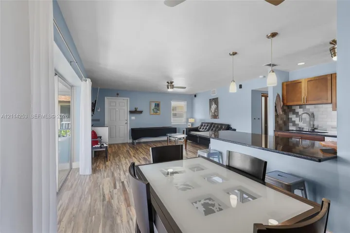 Open-concept interior featuring wood-finish flooring, a kitchen peninsula with a stone countertop, glass pendant lighting, and sliding glass doors