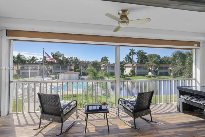 Screened balcony featuring wood-finish flooring, a ceiling fan, and metal railings, with water and pool area visibility