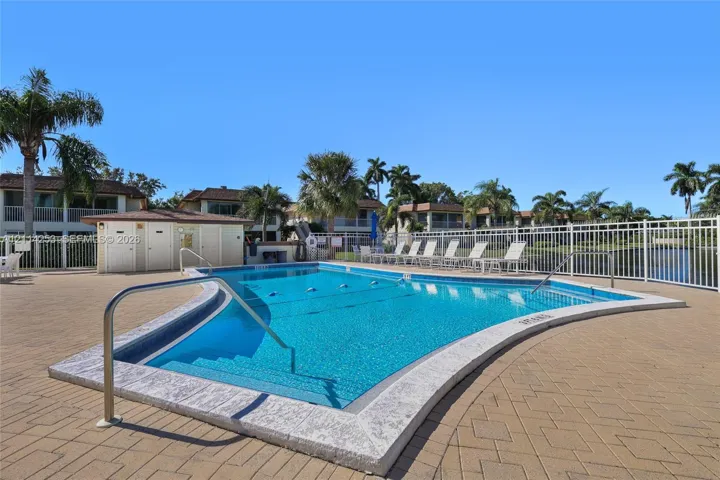 In-ground swimming pool featuring a curved concrete perimeter, metal handrails, and surrounding paver patio