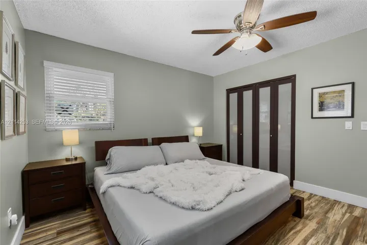 Wood-finish flooring, multi-pane window with adjustable blinds, ceiling fan with integrated light fixture, and closet with dark-finish frames and frosted glass panels