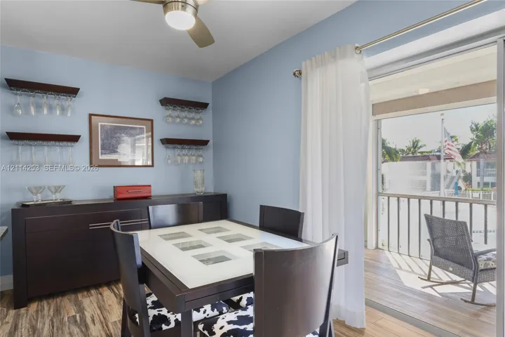 Dining area featuring wood-finish flooring, brushed nickel ceiling fan with integrated lighting, and wall-mounted wood shelving