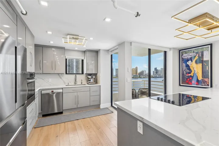 Kitchen featuring high-gloss cabinetry, stone-surface countertops, wood-finish flooring, stainless steel appliances, and integrated geometric lighting fixtures