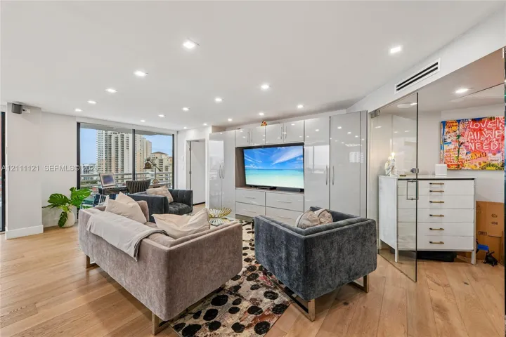 Open-concept interior featuring light wood-finish flooring, recessed lighting, floor-to-ceiling glass enclosure, and high-gloss built-in cabinetry with integrated media center