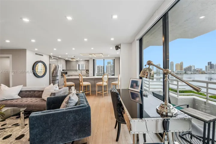 Open-concept interior featuring light-toned wood-finish flooring, recessed lighting, kitchen with stainless steel appliances and island, and expansive floor-to-ceiling glass wall