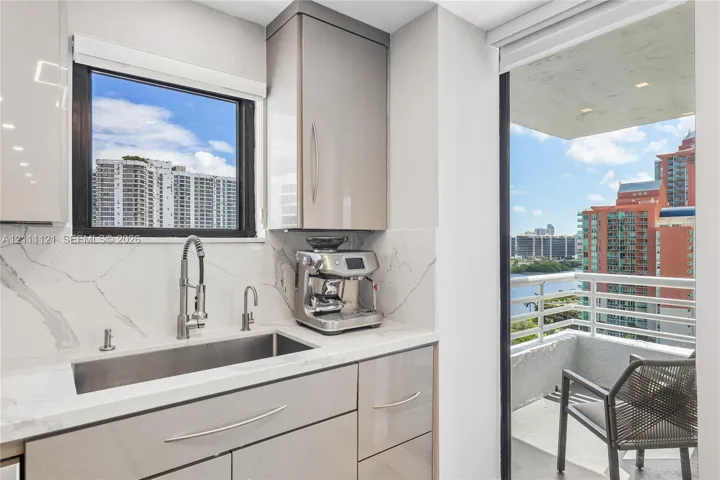 Glossy cabinetry featuring integrated hardware, stone-finish backsplash, undermount stainless steel sink with high-arc pull-down faucet, and access to a private balcony
