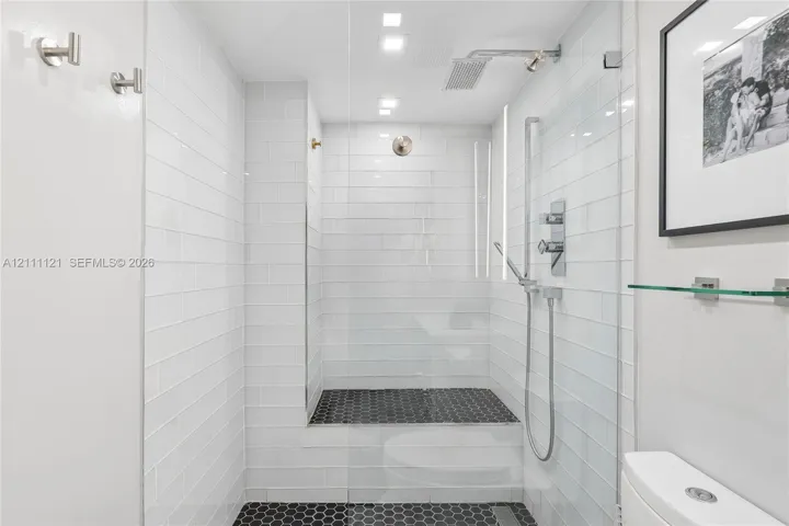 Walk-in shower featuring white subway wall tile, black hexagonal floor tile, glass enclosure, rainfall shower head, and hand-held shower fixture
