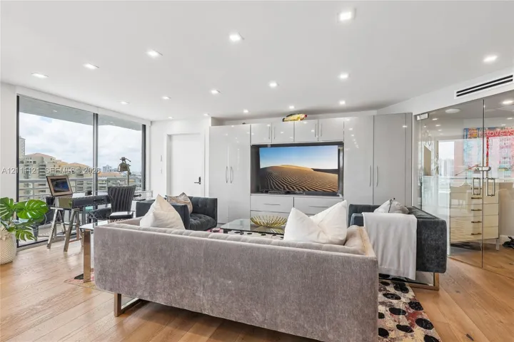 Living area featuring wood-finish flooring, recessed lighting, floor-to-ceiling windows, integrated white cabinetry, and a glass-enclosed partitioned space
