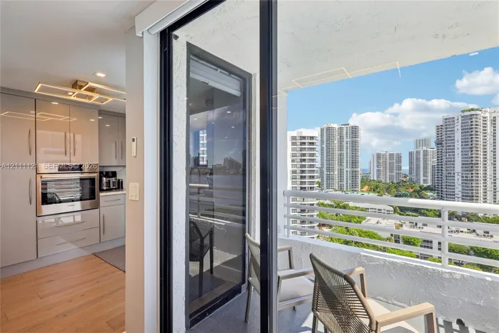 Kitchen featuring high-gloss cabinetry, stainless steel built-in wall oven, wood-finish flooring, and a balcony with a white metal railing and a cityscape backdrop