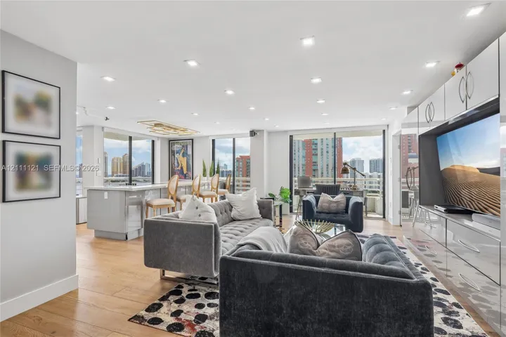 Open-concept main living area featuring wood-finish flooring, recessed lighting, floor-to-ceiling glass sliding doors, and custom built-in white cabinetry with integrated media storage