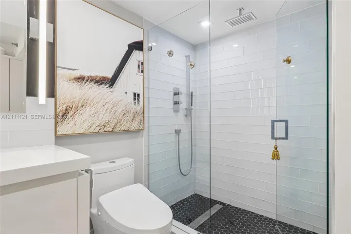 Walk-in shower featuring a frameless glass enclosure, white subway tile surround, dark hexagonal floor tiling, and a rainfall showerhead