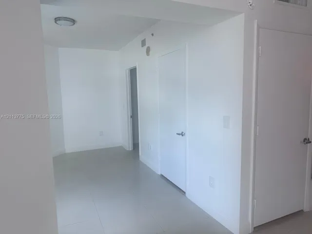 Interior space featuring neutral wall paint, polished tile flooring, white-finish interior doors with metallic hardware, and circular ceiling-mounted lighting
