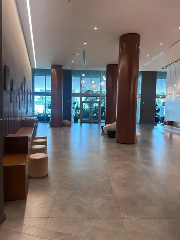 Expansive lobby featuring large-format tile flooring, full-height decorative wood-clad columns, built-in wooden bench seating, and floor-to-ceiling glass paneling
