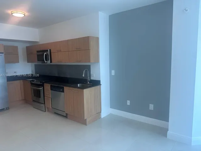 Kitchen featuring wood-finish cabinetry, dark solid-surface countertops, stainless steel appliances, and tile flooring