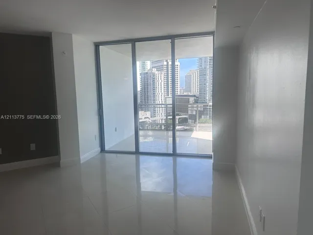 Floor-to-ceiling glass sliding doors, polished tile flooring, and a private balcony with an urban skyline backdrop
