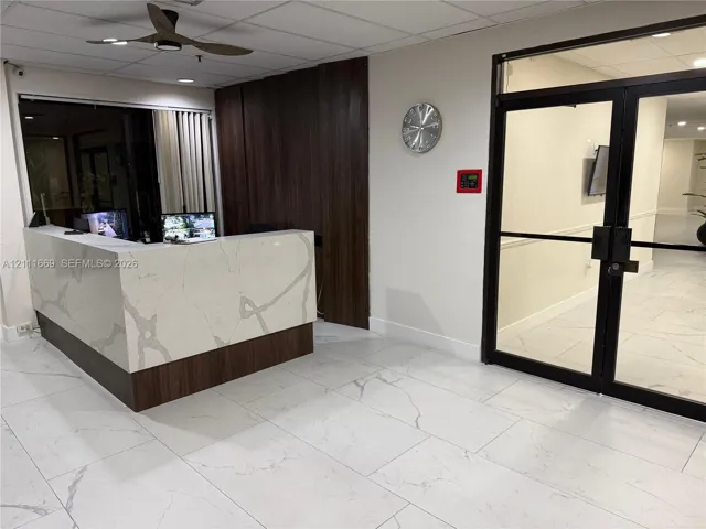 Reception area featuring a stone-surface desk with a wood-finish base, large-format tile flooring, dark wood-tone paneled wall cladding, and double glass doors with matte black frames