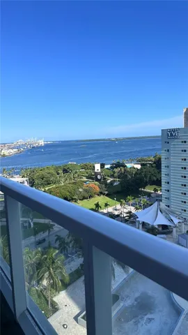 Balcony featuring a metal and glass railing, overlooking an expansive urban waterfront and park area