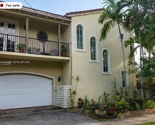 Stucco exterior featuring an arched-entry garage, wrought-iron railed upper balcony, barrel tile roofing, and arched windows