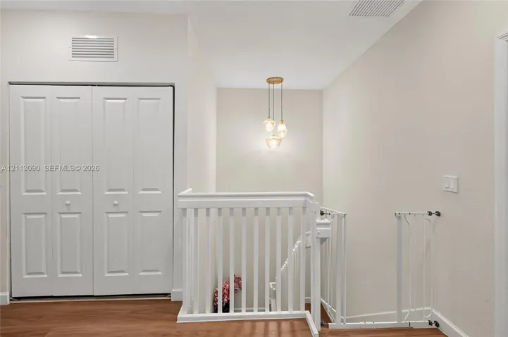 Wood-finish flooring, white paneled double-door closet, and decorative multi-light pendant fixture