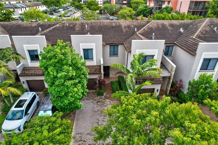 Multi-level townhome exterior featuring a tiled roof, stucco facade, paver driveway, and mature landscaping