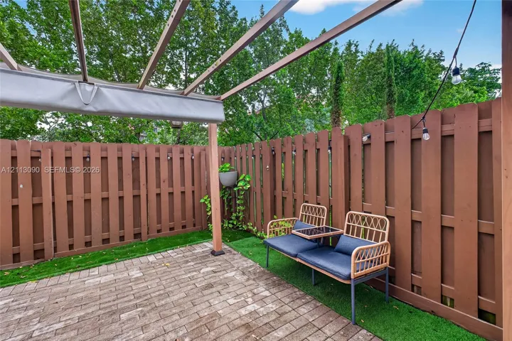 Outdoor patio featuring a brick paver surface, wooden pergola with a retractable shade canopy, artificial turf landscaping, and a solid wood privacy fence