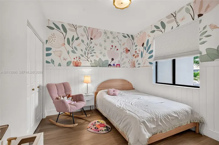 Bedroom featuring floral wallpaper, white vertical wall paneling, wood-finish flooring, and a pleated window shade