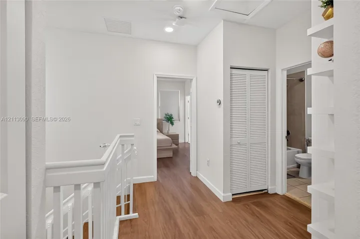 Hallway featuring wood-finish flooring, white wood railing, recessed lighting, white louvered closet doors, and built-in wall shelving