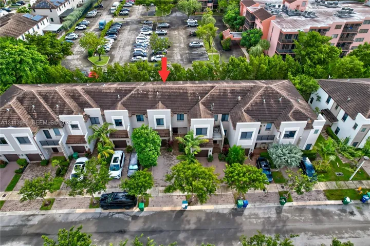 Multi-level townhouse exterior featuring a concrete tile roof, neutral stucco facade, individual garage bays, and mature landscaping