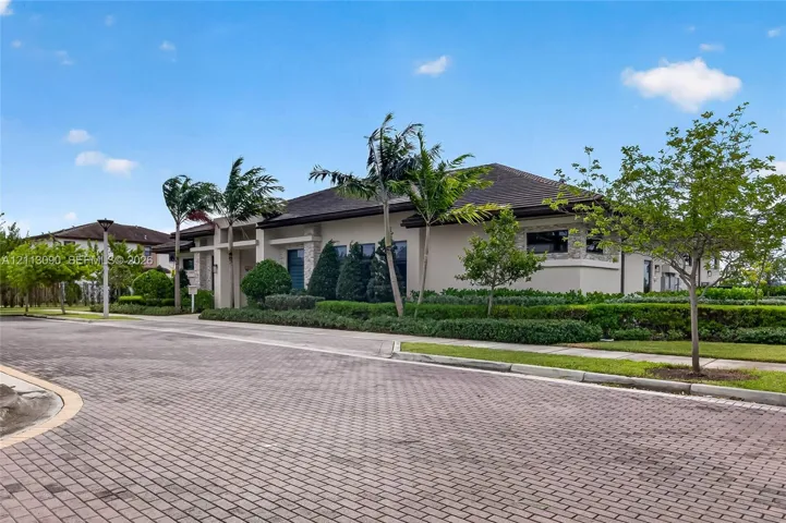 Single-story residence featuring a neutral stucco exterior, stone accent detailing, a hipped roof, and mature palm tree landscaping