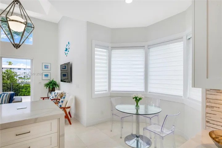 High-ceilinged room featuring a bay window, light-toned tile flooring, a geometric pendant light fixture, and a kitchen island with a stone-finish countertop