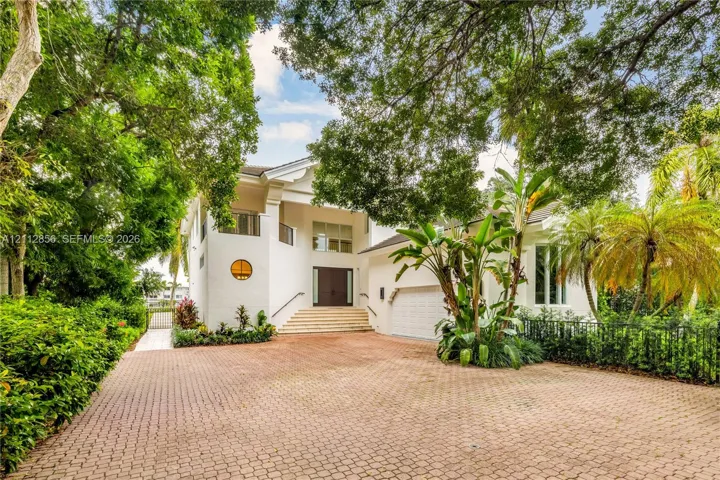 Stucco exterior featuring a circular accent window, elevated entryway with stone steps, multi-car garage, and a spacious paved driveway shaded by mature trees