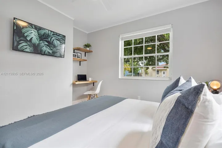 Neutral-toned room featuring a multi-pane window, built-in wooden wall shelving, and a wall-mounted desk