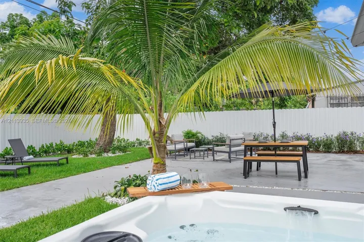Backyard featuring a hot tub, concrete patio, mature palm tree, manicured lawn, and white privacy fencing