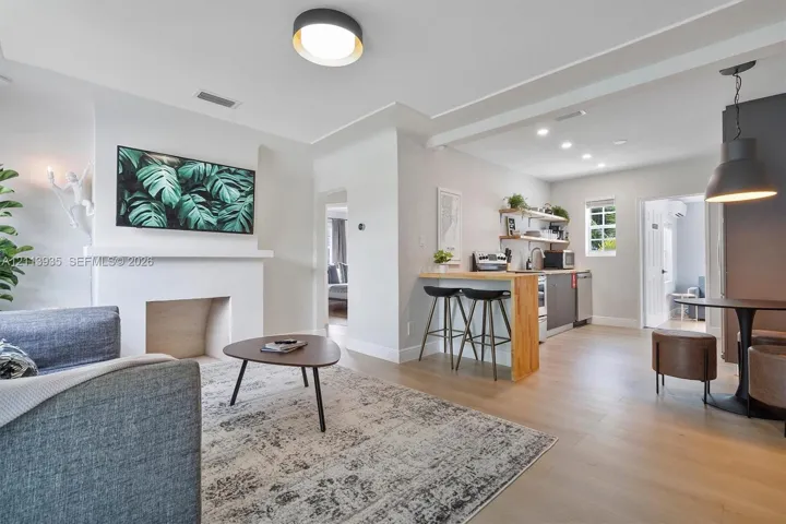 Open-concept interior featuring wood-finish flooring, a minimalist fireplace surround, built-in kitchen breakfast bar with wood countertop, recessed lighting, and metal pendant fixtures