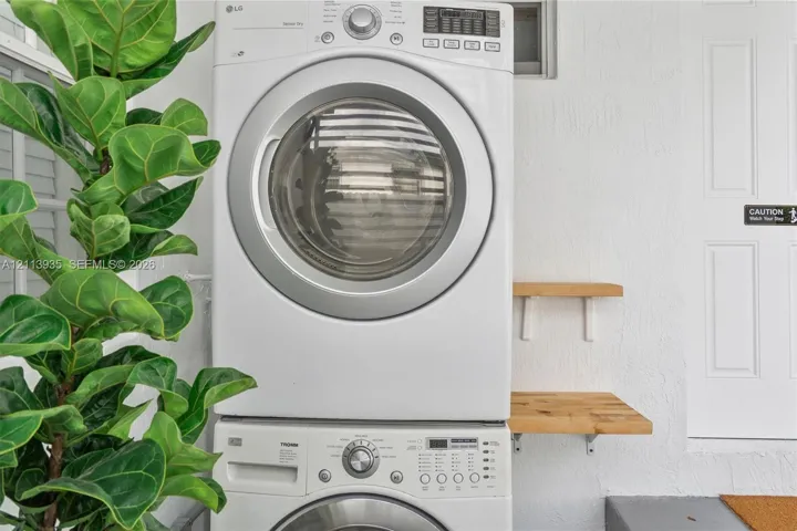 Stacked front-load washer and dryer unit with dual wood-finish wall-mounted shelving and white textured wall finish