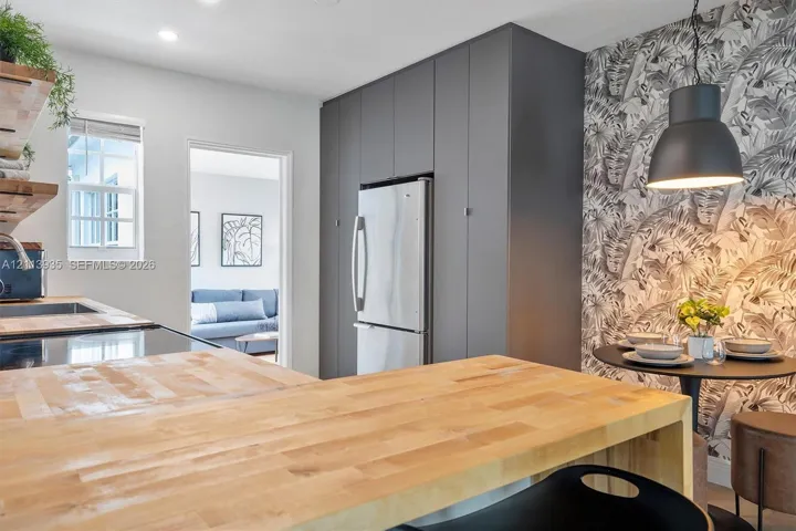 Kitchen featuring wood-finish butcher block countertops, floor-to-ceiling cabinetry, stainless steel refrigerator, patterned wall covering, and a matte black pendant light fixture