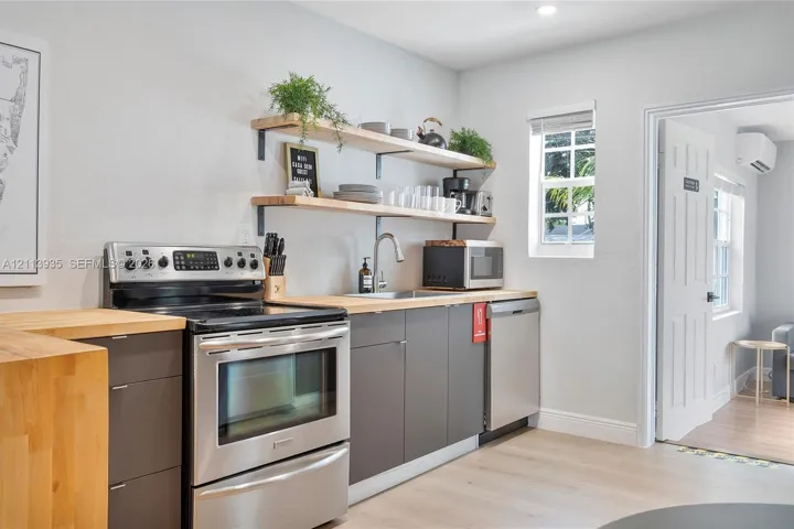 Kitchen featuring stainless steel appliances, butcher block countertops, dual-tier wall-mounted wood shelving, recessed lighting, and wood-finish flooring