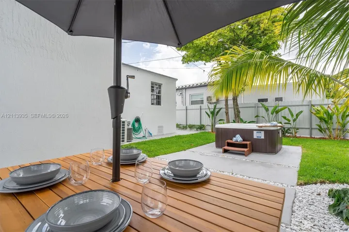 Rear exterior featuring a concrete patio, integrated hot tub, manicured lawn, and decorative stone landscaping border
